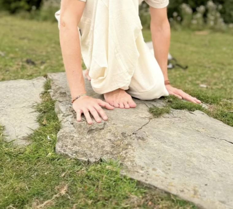 Hände und nackte Füße auf einem Stein im Gras